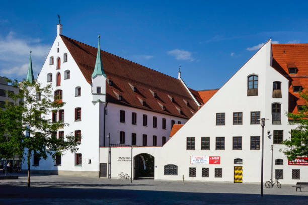 View of historic buildings and a clock tower with colorful shutters under a blue sky in Regensburg, Bavaria, Germany.