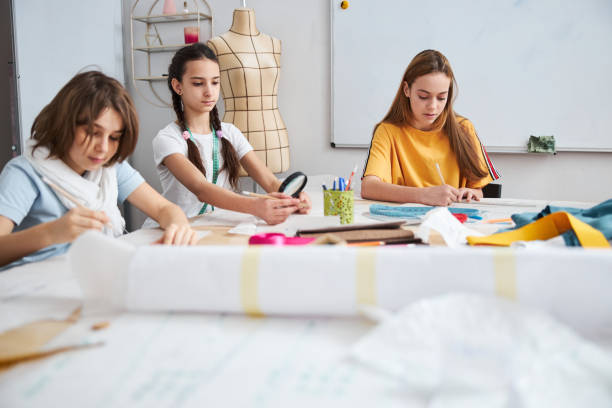 istock Cute girls drawing clothes patterns in sewing workshop 1309458118