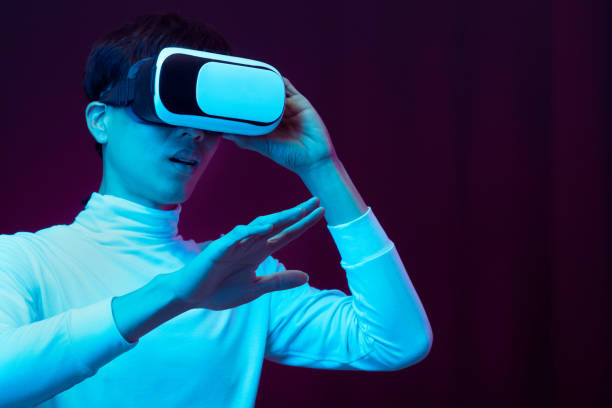 istock Excited asian young man wearing VR headset in neon light, Future technology concept 1309459215