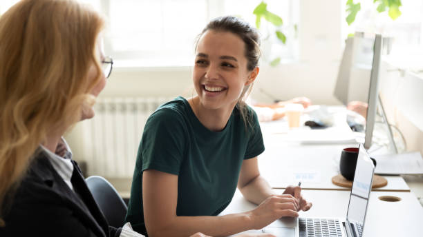 feliz aprendiz sonriente discutiendo ideas de negocios con entrenadora adulta - trainee fotografías e imágenes de stock