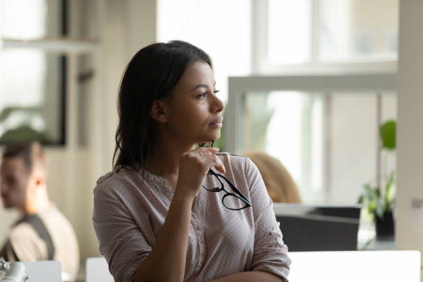 pensativa millennial biracial funcionária fazendo pausa olhando para a distância - pensive women business mature adult - fotografias e filmes do acervo