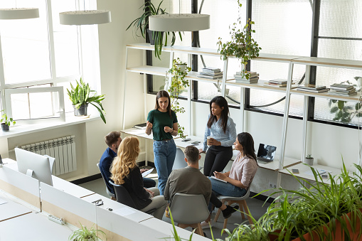Workshop at break time. Group of six focused concentrated diverse business people corporate staff employees executives listening to millennial woman team leader creating idea plan talking interacting