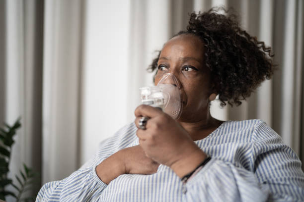 mature woman using an inhalation mask at home - oxygen imagens e fotografias de stock