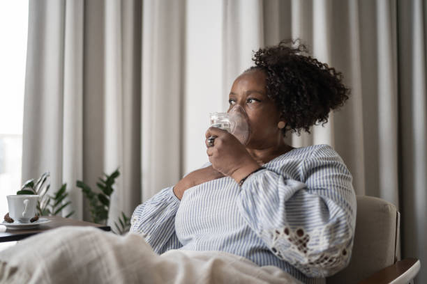 reife frau mit einer inhalationsmaske zu hause - nebulizer stock-fotos und bilder