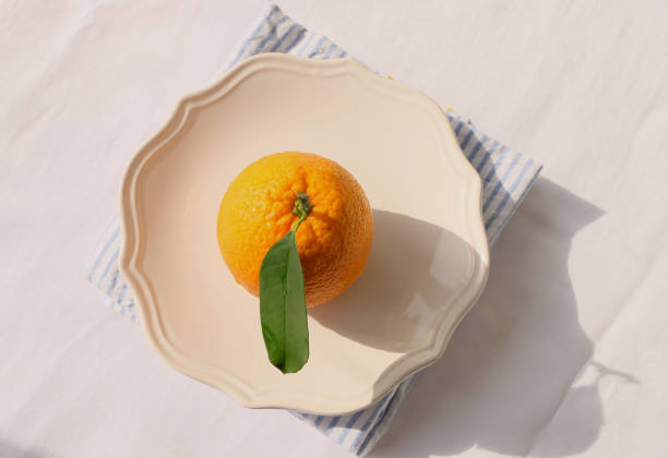istock One ripe orange with green leaves in beige ceramic plate, White tablecloth 1309472008