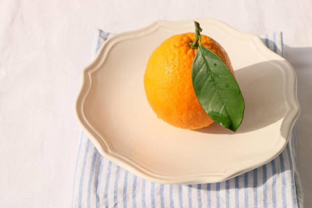 istock One ripe orange with green leaves in beige ceramic plate, White tablecloth, Front view 1309472029