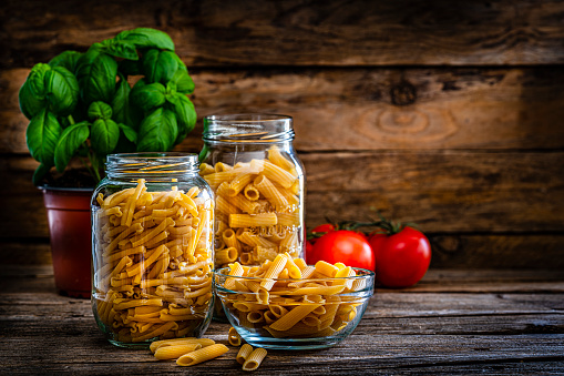 Italian food: front view of various types of uncooked pasta in glass jars shot on rustic kitchen table. The composition is at the left of an horizontal frame leaving useful copy space for text and/or logo at the right. High resolution 42Mp studio digital capture taken with Sony A7rII and Sony FE 90mm f2.8 macro G OSS lens