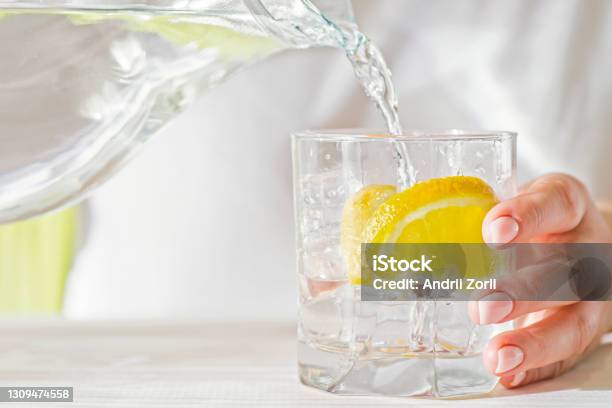 Female Hands Pouring Water From The Decanter Into A Glass Beaker With Lemon And Ice Health And Diet Concept Quenching Thirst On A Hot Day Stock Photo - Download Image Now