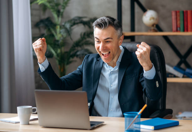 istock Overjoyed gray-haired caucasian business leader, programmer or ceo, dressed in formal wear, sits in the office, rejoices at success, victory or good profit, looks at a laptop and gestures with hands 1309478244