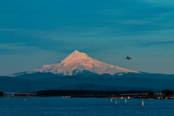 A plane takes off over Mt Hood from Portland International Airport as sailboats sail in the Columbia River
