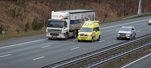 Zeist, province Utrecht, Netherlands, february 27th 2017, Dutch yellow Volkswagen ambulance overtaking a DAF truck on the A-28 highway near Zeist at daytime as seen from a viaduct - at this point, the highway is three laned at both sides, divided by crahs barriers - the A-28 is some 188 kilometers long between the city of Groningen in the north and the city of Utrecht in the middle of the country