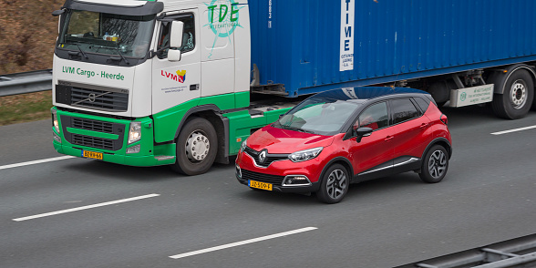 Zeist, province Utrecht, Netherlands, february 27th 2017, Dutch red 2016 Dutch Renault Captur crossover SUV overtaling a Volvo truck on the A-28 highway near Zeist at daytime as seen from a viaduct - at this point, the highway is three laned at both sides, divided by crahs barriers - the A-28 is some 188 kilometers long between the city of Groningen in the north and the city of Utrecht in the middle of the country