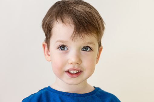 Close up portrait of 3 year old child boy with blond hair in blue t-shirt on white background