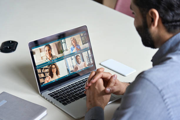 istock Indian business man having virtual team meeting on video conference call using laptop work from home office talking to diverse people group in remote teamwork online distance chat. Over shoulder view 1309489749