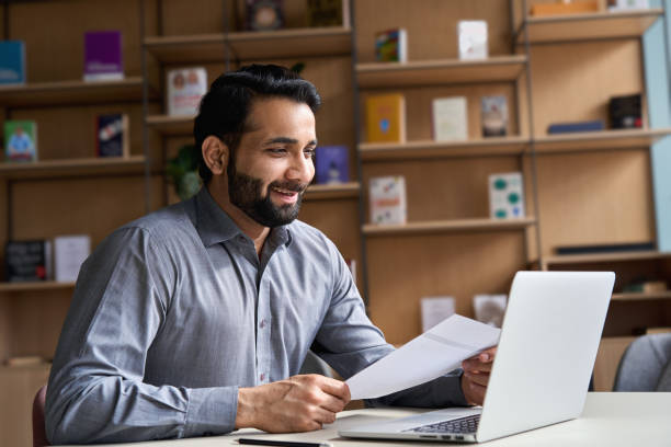 Smiling indian business man hr employer, teacher or lawyer holding cv document having virtual job interview meeting by video conference call, consulting client on laptop at online legal advice. sonriente hombre de negocios indio hr empleador, profesor o abogado que sostiene documento cv teniendo una entrevista virtual de trabajo reunión por videoconferencia, consultando al cliente en el ordenador portátil en el asesoramiento legal en línea.