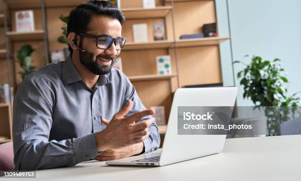 Happy Indian Business Man Remote Teacher Customer Support Manager Wearing Headset Talking At Virtual Meeting Consulting Client On Video Call Giving Distance Learning Class At Home Office Call Center Stock Photo - Download Image Now