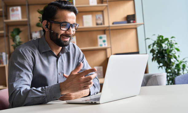 快樂印度商人遠端老師，客戶支援經理戴著耳機在虛擬會議諮詢客戶端視頻通話給遠端學習類在家裡的辦公室呼叫中心。 - 偏遠的 個照片及圖片檔