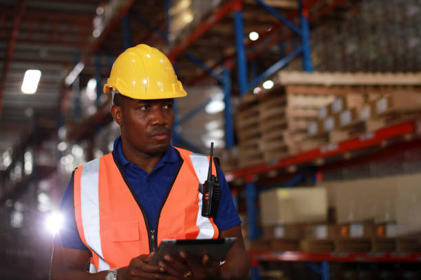 verticale beau gilet de sécurité de robe de travail et tablette de retienne de casque de sécurité travaillant dans l’entrepôt et l’usine - réhabilitation industrielle photos et images de collection