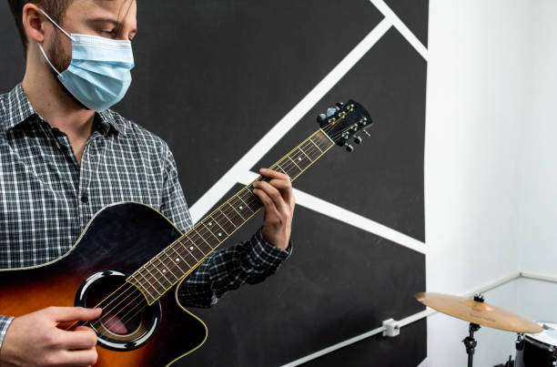 istock Young musician in protective mask practicing in playing guitar by focusing on hand and chords. 1309498420