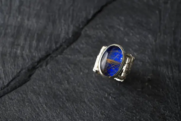 Extreme close-up of rutile quartz with lapis lazuli ring on a black slate.