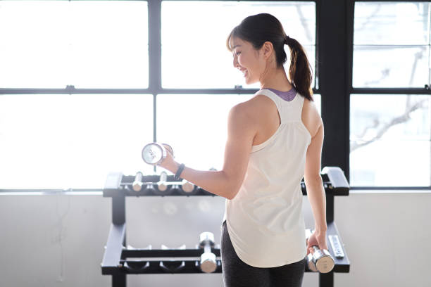 asian woman with dumbbells in a training gym - people vibrant color sunlight cheerful imagens e fotografias de stock