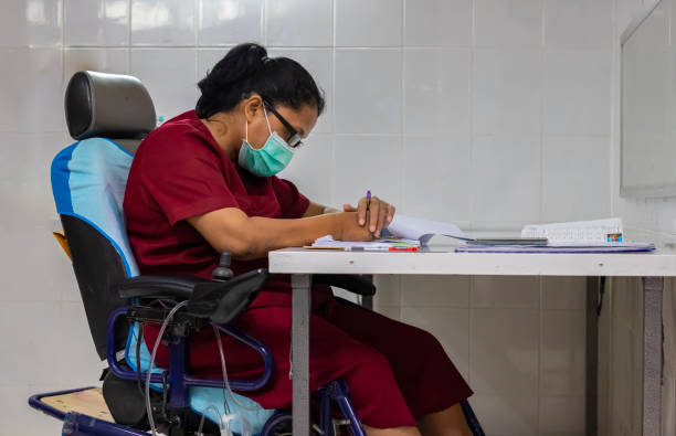 una mujer con quadriplegia sentada en su silla de ruedas eléctrica mientras usaba sus dos manos haciendo papeleo en el escritorio de su oficina. - cuadriplégico fotografías e imágenes de stock