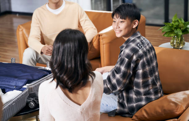 Asian kid and parents sitting in living room smiling talking to each other when packing suitcase preparing for travel stock photo