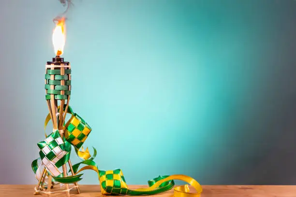 Traditional Malay torch and decorative ketupat lit up during Hari Raya Aidilfitri celebration against green background