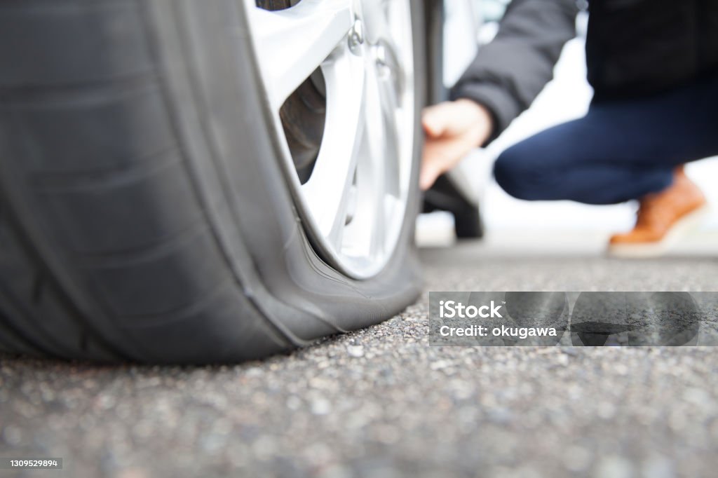 man touching a flat tire on the roadside Flat Tire Stock Photo
