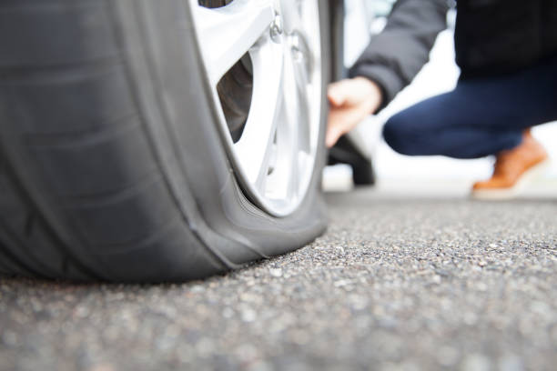 man touching a flat tire on the roadside - deflated imagens e fotografias de stock