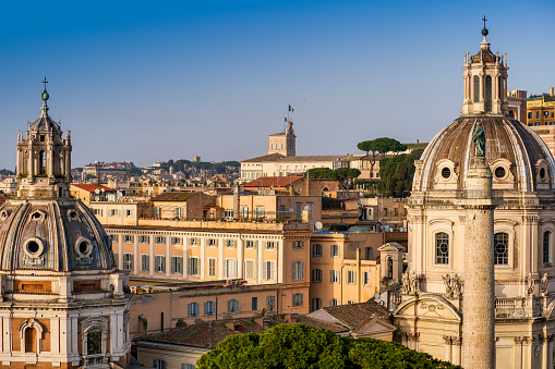The horizon over the rooftops of the historic center of Rome from the panoramic terrace of the Altare della Patria National Monument, in the heart of the Eternal City. In the foreground the domes of the church of Santa Maria di Loreto (left) and the church of the Santissimo Nome di Maria al Foro, with the Trajan's column (right). In the background the Quirinal Hill and the Presidential House with the Italian flag on top. Image in high definition format.