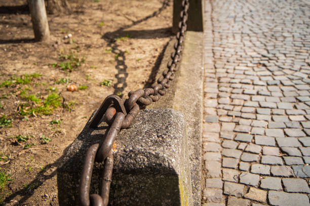 a fence with a rusty chain near a stone road, decorative\n coarse chain fence, ancient coarse links, old town architecture