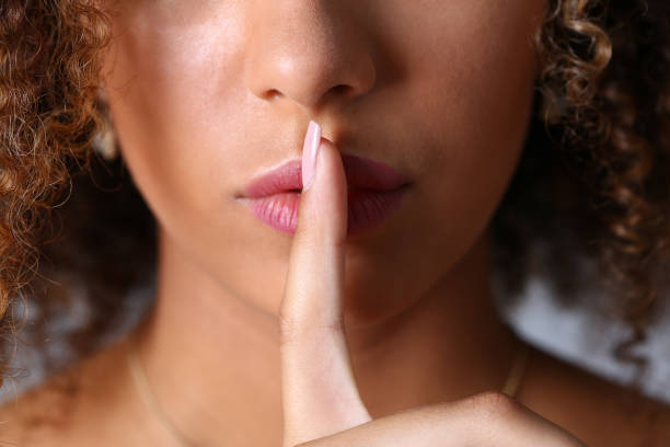 istock Curly young woman holding index finger at lips 1309534601