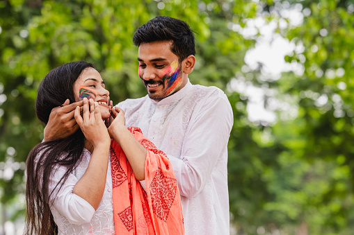Happy fun loving Asian / Indian couple painted in colors or gulal and celebrating holi festival outdoor. Concept of Indian festival Holi with Indian Couples.
