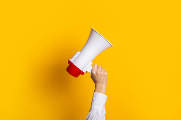 istock female hand holds a white with a red megaphone on a yellow background. 1309537138