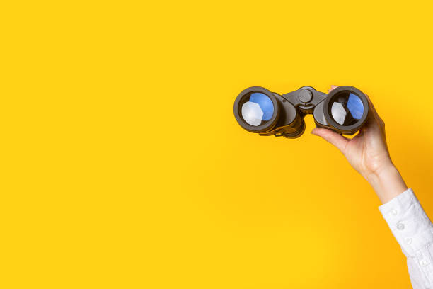 female hand holds black binoculars on a bright yellow background female hand holds black binoculars on a bright yellow background. binoculars stock pictures, royalty-free photos & images