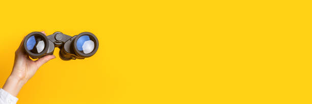 istock female hand holds black binoculars on a bright yellow background. Banner 1309537251