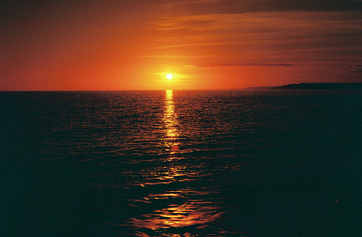 The sun setting over the horizon and reflections in the sea, lomography redscale 35mm film