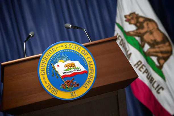 Photo of Press conference of governor of the state of California concept. Seal of the governor of the State of California on the tribune with flag of USA and California state.