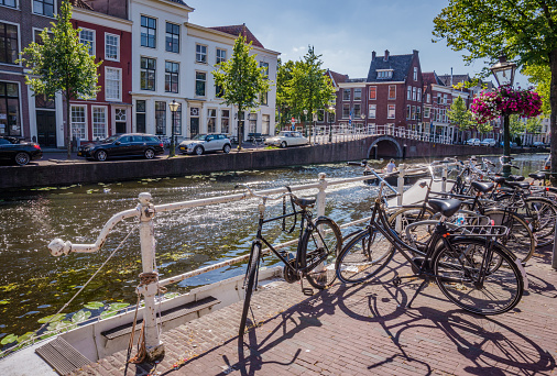 Leiden, the Netherlands - June 27, 2018: Bunch of bicycles standing by a canal in city centre of Leiden, Holland on a bright Summer day. Dutch old buildings facade view.