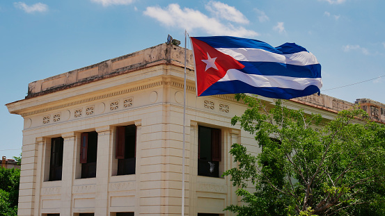 Flag of Cuba on a flagpole blowing in the wind, with a building in the background