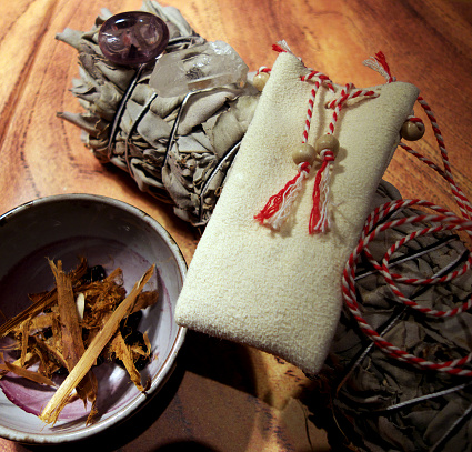 Necessities for a small spiritual ritual. A small suede medicine bag, dried sage, a piece of cut rock crystal, a purple amethyst, pieces of palo santo wood. Selective focus.