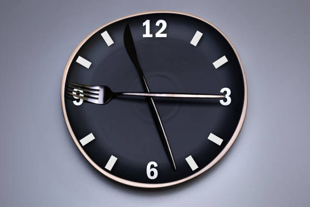 istock Clock on the black plate, with cutlery, grey background. The concept of intermittent fasting, lunchtime, diet and weight loss. 1309557721