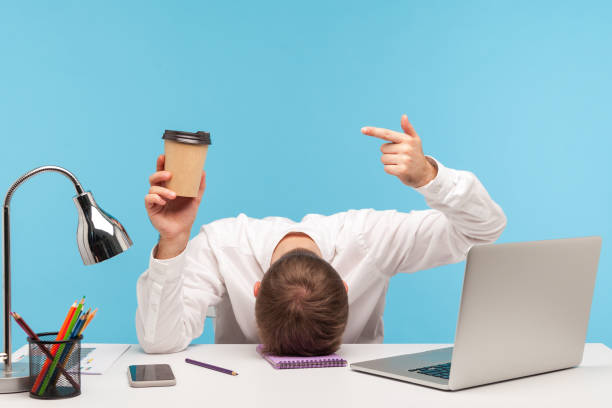 istock I need more coffee. Tired business man lying on table face down and pointing at paper cup in his hand, lack of energy, overworking 1309558758