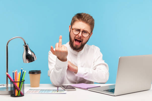 istock Excited rude man with beard office worker showing middle finger looking at camera sitting at workplace, uncultured gesture, disrespect and negativity 1309558774