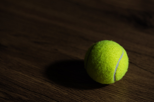 Light and shadow style photo of a tennis ball on the wooden floor.
