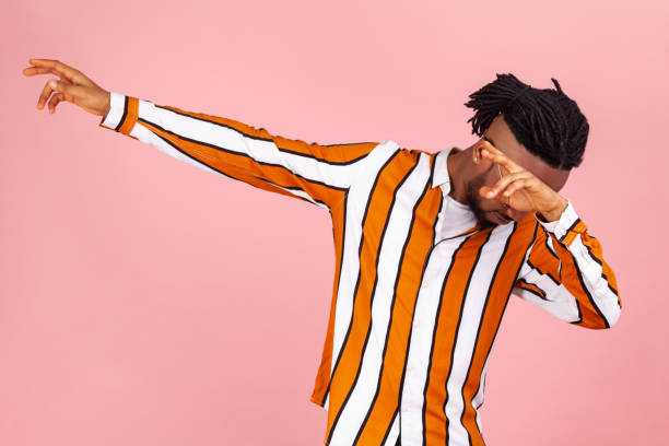 Trendy afro-american man with dreadlocks in bright striped shirt making dab dance move, imitating famous internet meme, expressing triumph Trendy afro-american man with dreadlocks in bright striped shirt making dab dance move, imitating famous internet meme, expressing triumph. Indoor studio shot isolated on pink background dab dance stock pictures, royalty-free photos & images