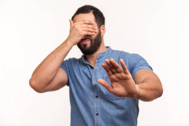 Scared confused man with beard closing eyes with palm of hand, stretching out another hand forward touching space, looking for way in darkness