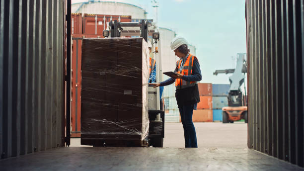 motorista de empilhadeira carregando um contêiner de carga de transporte com uma palete completa com caixas no terminal portuário logístico. supervisora industrial latina e inspetora de segurança com gerenciamento de tablets do processo. - distribution warehouse forklift freight transportation pallet - fotografias e filmes do acervo