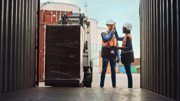 istock Forklift Driver Loading a Shipping Cargo Container with a Full Pallet with Boxes in Logistics Port Terminal. Latin Female Industrial Supervisor and Safety Inspector with Tablet Giving Him High Five. 1309560047
